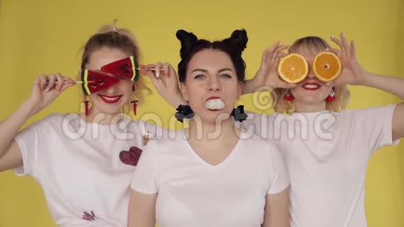 三个女孩在黄色背景下玩得很开心嚼口香糖玩糖果和水果视频的预览图