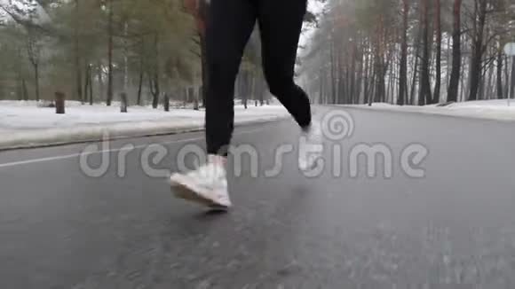 年轻迷人的白种人女孩在冬天带着耳机在雪地公园跑步特写双腿前方跟进射击视频的预览图