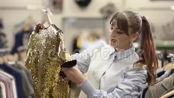 一位年轻漂亮的女士在一家服装店里展示和试穿一件金色火花的连衣裙视频的预览图