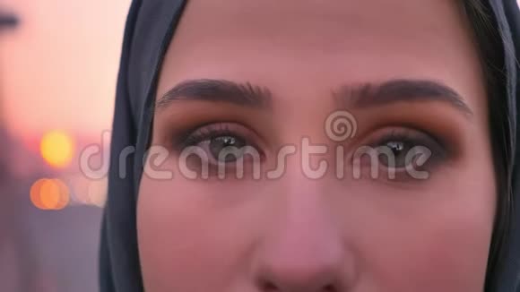 年轻美丽的穆斯林女性灰色眼睛的特写肖像直视镜头背景是城市视频的预览图