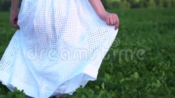 穿着白色连衣裙的女人或少女走在绿色的田野上用手拿着连衣裙视频的预览图