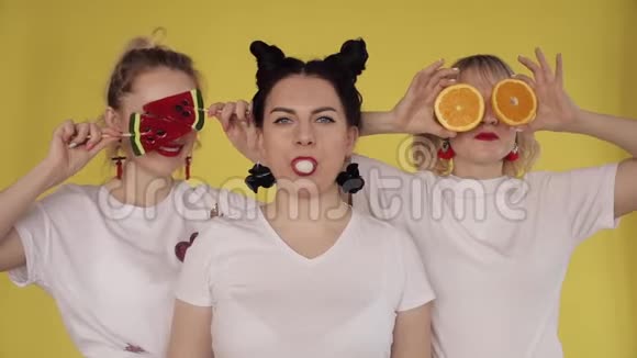 三个女孩在黄色背景下玩得很开心嚼口香糖玩糖果和水果视频的预览图