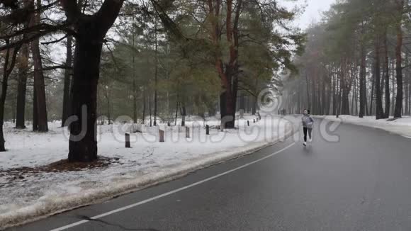 年轻迷人的白种人女孩在冬天带着耳机在雪地公园跑步前面的静态镜头慢动作视频的预览图