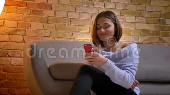一位年轻可爱的白种人女性使用电话和微笑坐在舒适的室内地板上的特写镜头视频的预览图