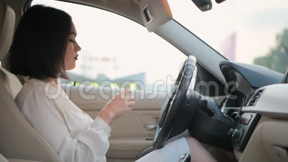 年轻漂亮优雅的黑发商务女性坐在一辆停着的车里用汽车的镜子涂口红视频的预览图