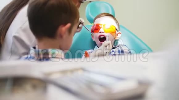 女牙医驾驶一个工具在一个病人的嘴男孩那个男孩他哥哥站在附近视频的预览图