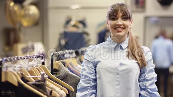 快乐迷人的女人站在衣服附近的服装店里微笑着视频的预览图