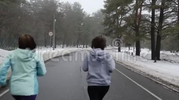 快乐的年长和年轻的高加索女人在冬天的雪地公园里奔跑交谈和微笑后退静态镜头视频的预览图