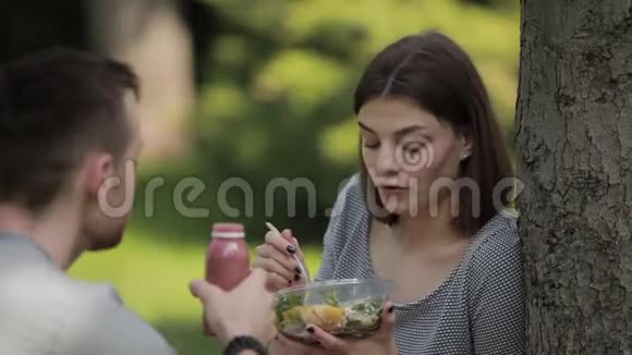 年轻的素食夫妇坐在公园里吃沙拉和喝冰沙视频的预览图