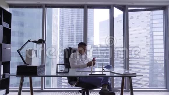漂亮的黑发男人穿着白色衬衫坐在现代办公室的玻璃办公桌后面视频的预览图