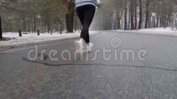 年轻迷人的白种人女孩在冬天带着耳机在雪地公园跑步关闭后跟射击慢动作视频的预览图