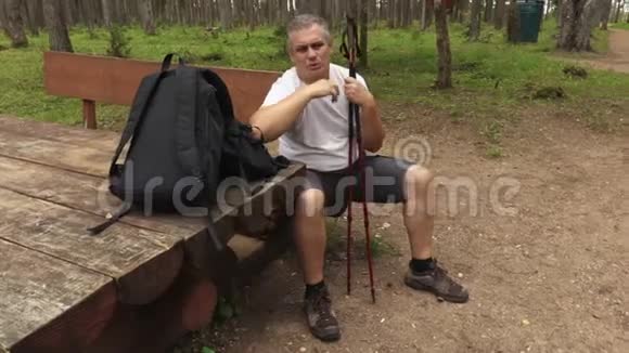 疲惫的徒步旅行者拿着拐杖在公园里长椅上休息视频的预览图
