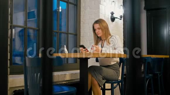 年轻女子晚上在餐厅使用电话应用程序和喝咖啡视频的预览图