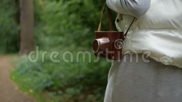 春天一个穿着棕色相机在树林里散步的女人视频的预览图