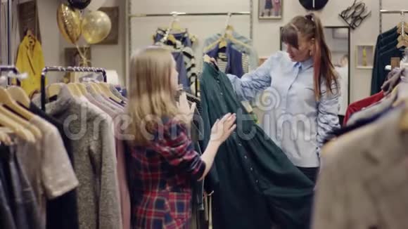 年轻可爱的女售货员试图在一家服装店向有吸引力的成年女性顾客出售一件连衣裙视频的预览图