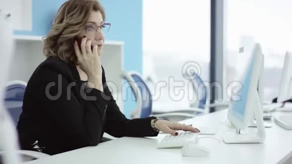 年轻的休闲女士坐在办公桌前用笔记本电脑接电话打电话微笑着在手机上说话视频的预览图