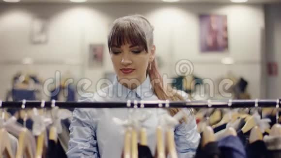 一位漂亮的年轻女士在服装店的货架上寻找衣服并检查黑色衬衫视频的预览图