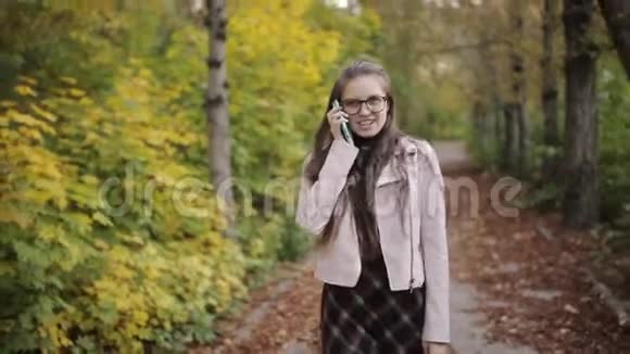 迷人的女孩少年n带着一本书在手机上聊天在美丽的秋天公园散步快乐女孩视频的预览图