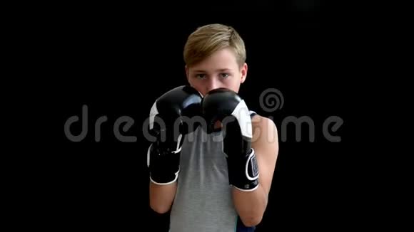 一个十几岁的拳击手正在做运动手套和灰色T恤在黑暗的背景这个男孩有一头金发和棕色视频的预览图