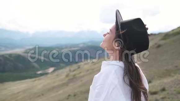 漂亮的黑发女人戴着帽子和白色衬衫在山里享受着大自然戴帽子的年轻女子的肖像视频的预览图