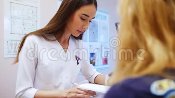 女牙医看病人的医学书书上是坐在对面的一位妇女看牙医视频的预览图