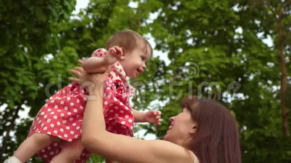 妈妈和小女儿在公园里玩笑妈妈把快乐的孩子扔到树的背景上慢慢视频的预览图