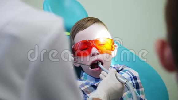 小男孩戴着黄色眼镜坐在椅子上这时牙医治疗他的牙齿病人视频的预览图