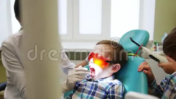 一位年轻的女牙医治疗一个小男孩牙齿另一个男孩病人他的兄弟玩得很开心分散了他的注意力视频的预览图