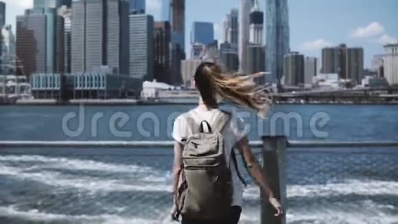 镜头跟随年轻快乐的旅行女孩背着背包在纽约曼哈顿天际线上张开双臂跳跃视频的预览图