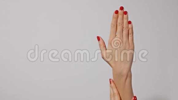 美丽的年轻女子她的手上有鲜红的指甲一只手轻轻地按摩另一只手被隔离在灰色的背景上视频的预览图