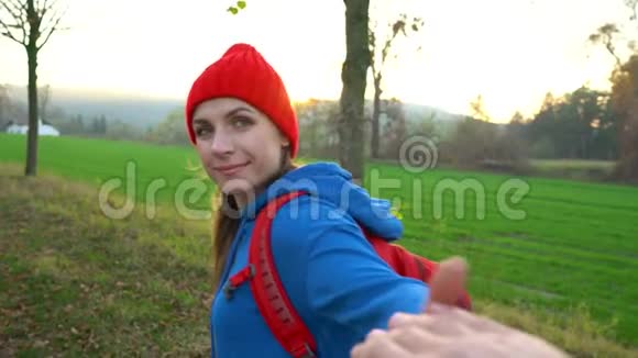 跟着我快乐的年轻女人戴着红帽子拉着男人手手牵手走在农村的田野里视频的预览图
