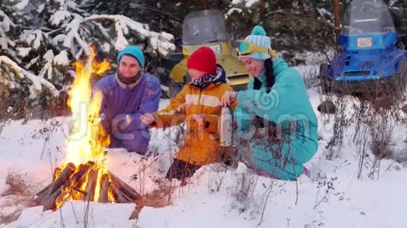 冬季森林一家人坐在火边的树林里在白天聊天煎香肠视频的预览图
