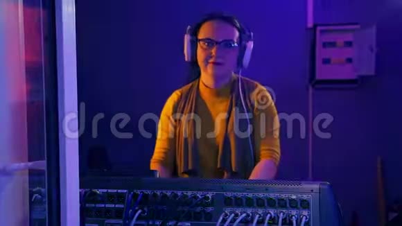 一个带耳机的女DJ在一个技术室在一个混合控制台在迪斯科的灯光下进行迪斯科视频的预览图