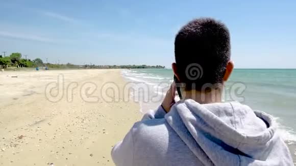 在希腊的哈尔基迪基年轻人看着大海用手机在沙滩上聊天视频的预览图
