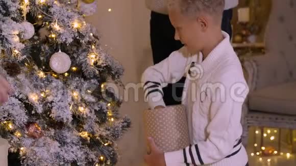 快乐少年用玻璃玩具和花环装饰圣诞树视频的预览图