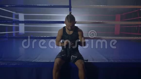 漂亮的拳击手在拳击比赛前用黑色绷带卷起来坐在拳击台附近视频的预览图