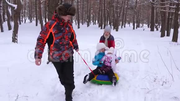 爸爸带着小宝宝坐在雪橇上穿过松树公园笑了起来在圣诞节假期家人可以放松视频的预览图