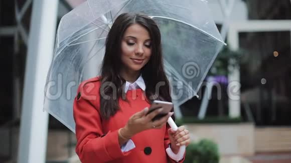 穿红色外套的商务女士在户外与移动助理交谈时在智能手机上发送音频语音信息她抱着她视频的预览图