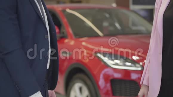 无法辨认的西装男人把钥匙给了穿粉色夹克的女人背景中的红色汽车汽车推销员视频的预览图
