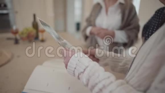 年长的女人的手向朋友展示她在厨房里的老白和黑照片背景模糊视频的预览图