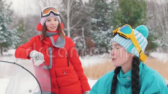 冬天一个穿着红色夹克的年轻女子站在雪地摩托上用一只手一个穿着蓝色夹克的年轻女子视频的预览图