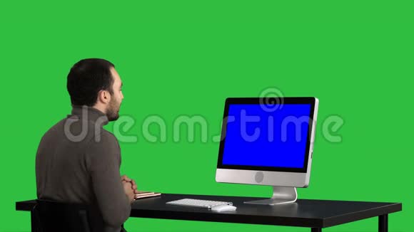 年轻的商人在绿色屏幕上的电脑上打视频电话色度键蓝色屏幕模拟显示视频的预览图