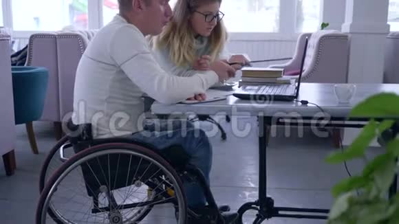 残疾人教育女教师眼镜为坐轮椅的残疾人男子使用笔记本电脑上课视频的预览图