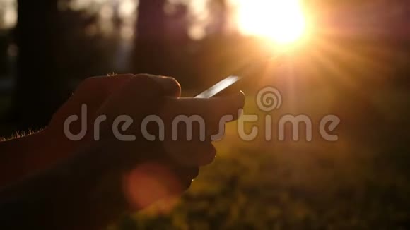 人类使用智能手机在日落时分在公园里打印一个信息特写相机移动视频的预览图