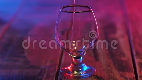 站在桌子上的玻璃杯里五颜六色的灯光倒着干邑慢动作视频的预览图