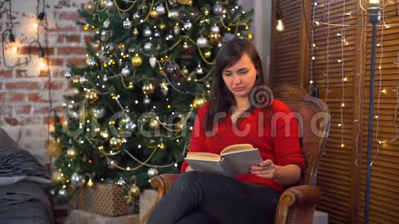 在圣诞树附近看书的年轻女子视频的预览图