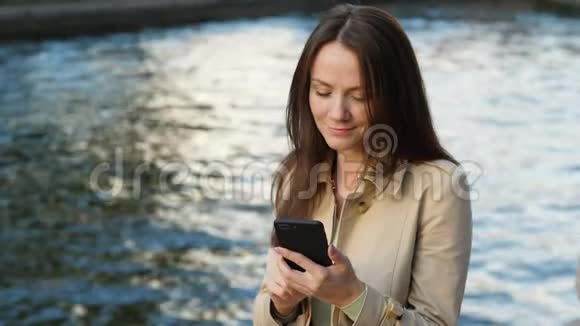 自由职业者女人在智能手机上浏览坐在河边的水上视频的预览图
