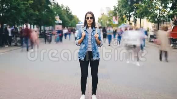 女性旅行者穿着墨镜和休闲服装背着背包站在大街上的时间推移放大视频的预览图