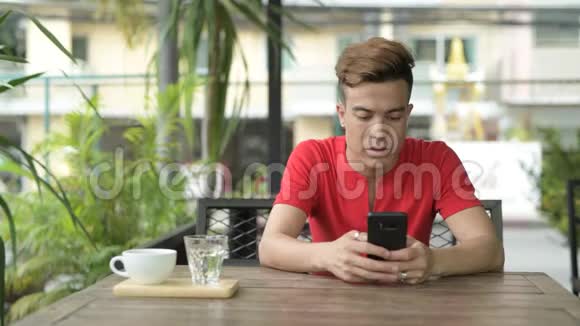 快乐的亚洲年轻人在户外咖啡店用电话视频的预览图