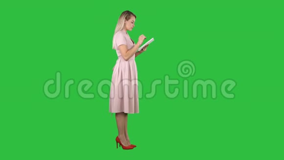 年轻女性穿着粉红色的裙子侧面视图使用平板电脑上的绿色屏幕铬键视频的预览图